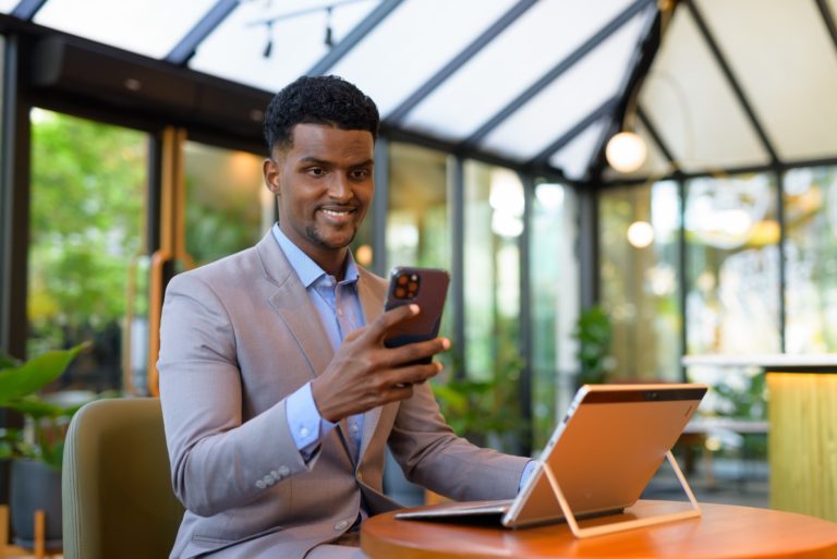 happy african businessman having virtual webinar meeting at coffee shop using laptop computer and mobile phone